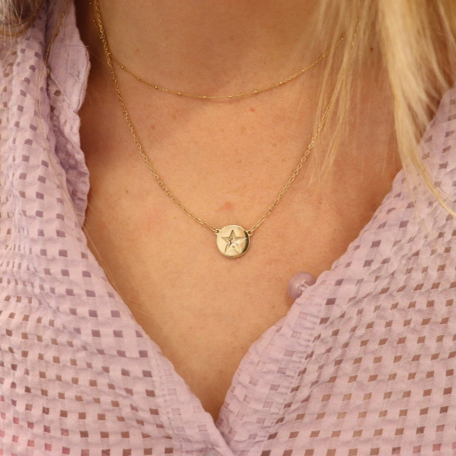 9ct gold star disc necklace on a woman's neck